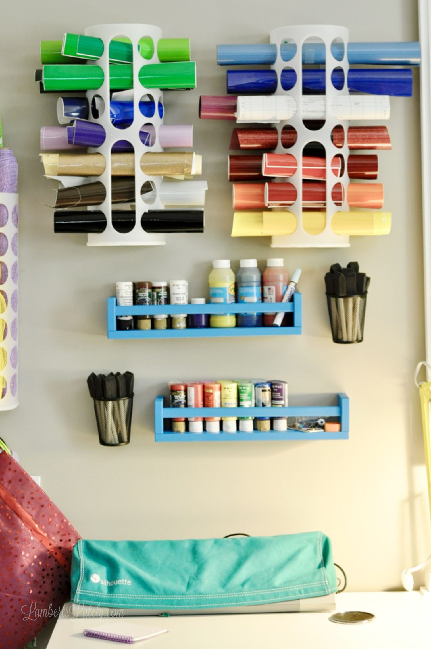 blue wooden shelves filled with paint jars, cutting vinyl organized on wall above