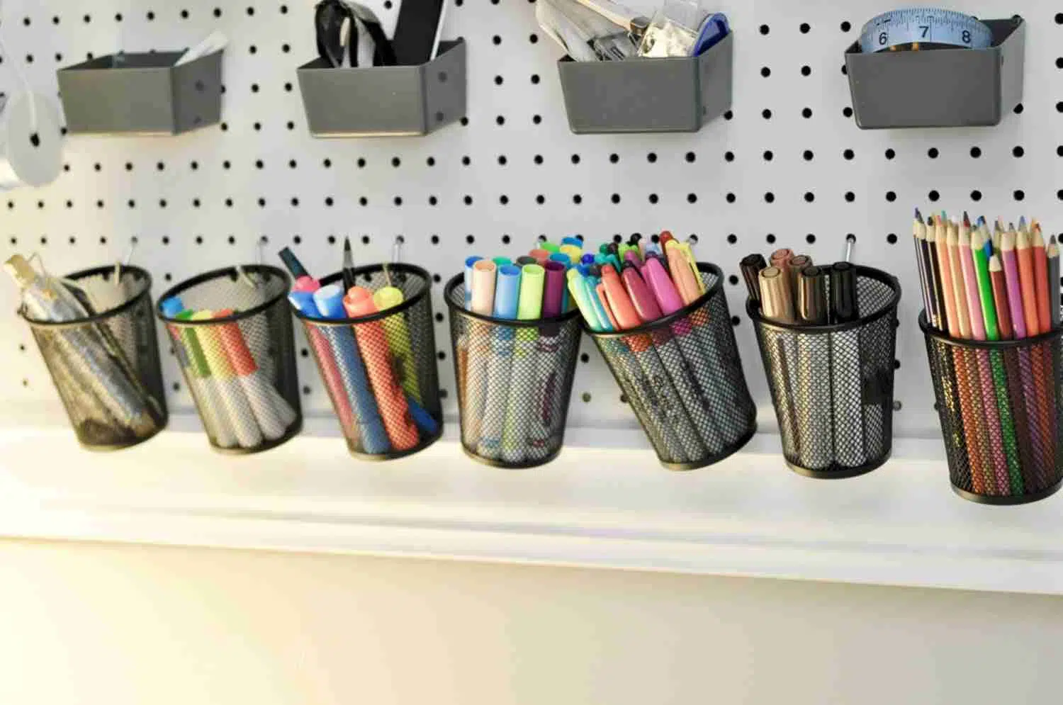 metal baskets hanging on a peg board with markers, pens, etc.
