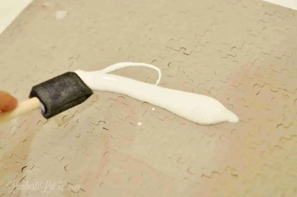 spreading mod podge on a puzzle with a sponge brush.