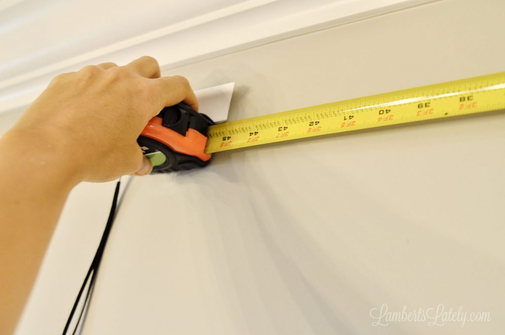 measuring molding on a wall with a tape measure.