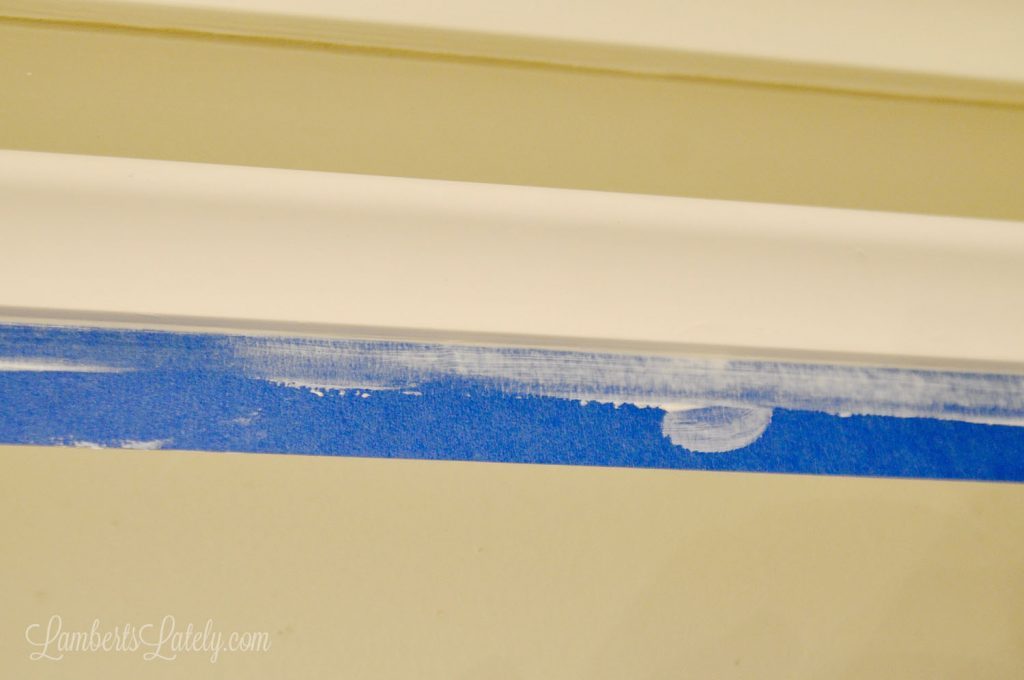 coat of caulk on bottom part of molding, with blue painters tape blocking wall.