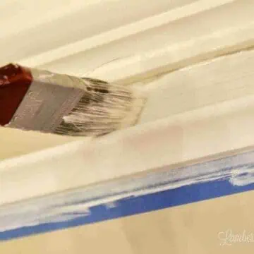 paint brush painting white paint in a gap between two pieces of crown molding on a wall.