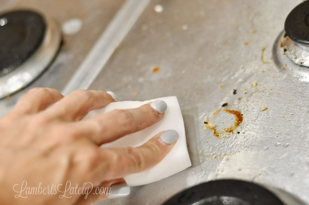 scrubbing stainless steel stovetop with a melamine sponge