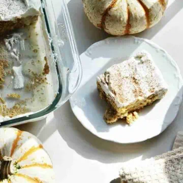 piece of pumpkin tres leches cake on a plate next to a baking dish and pumpkins.