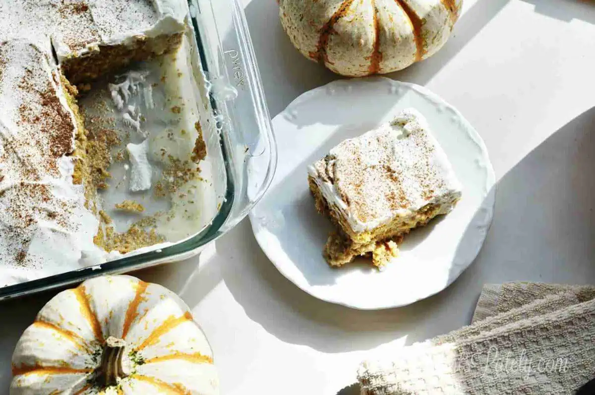 piece of pumpkin tres leches cake on a plate next to a baking dish and pumpkins.