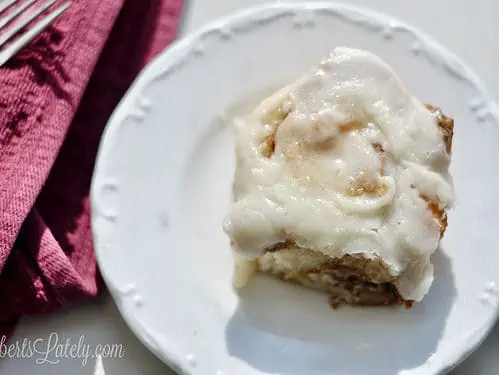 looking down on a cinnamon roll on a white plate with a red napkin.