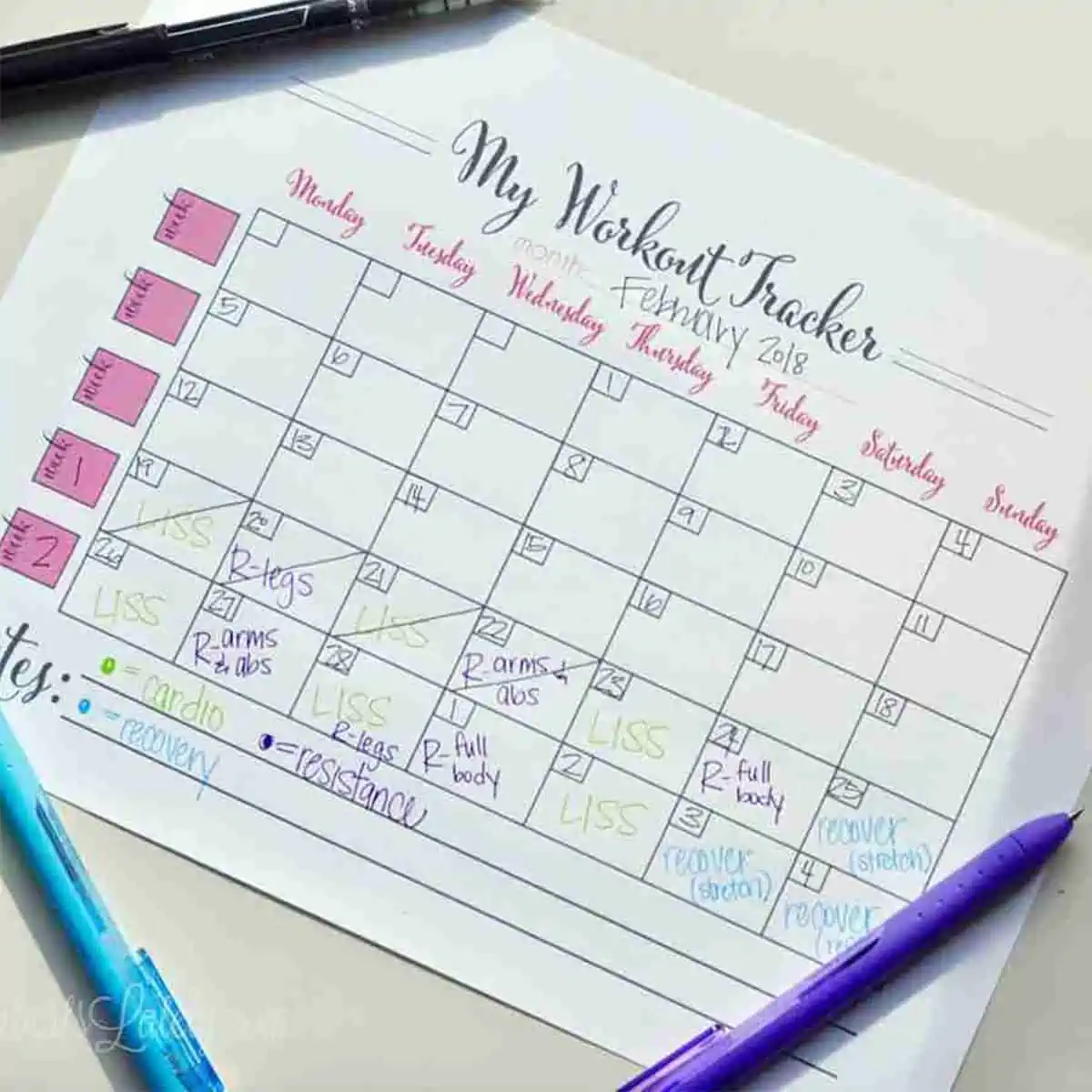 free printable workout calendar on a desk surrounded by pens