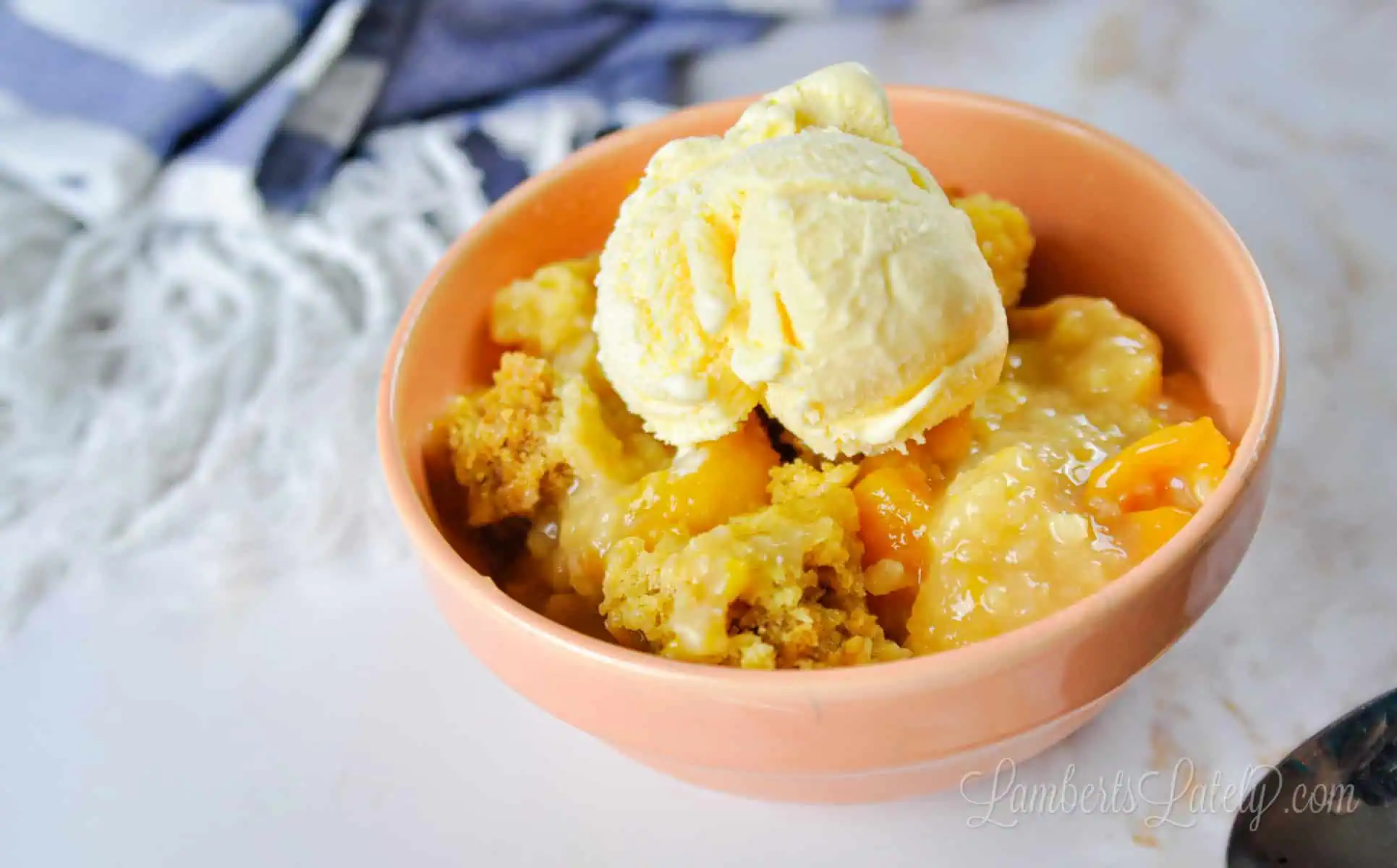 bowl of peach cobbler in front of a blue striped towel.