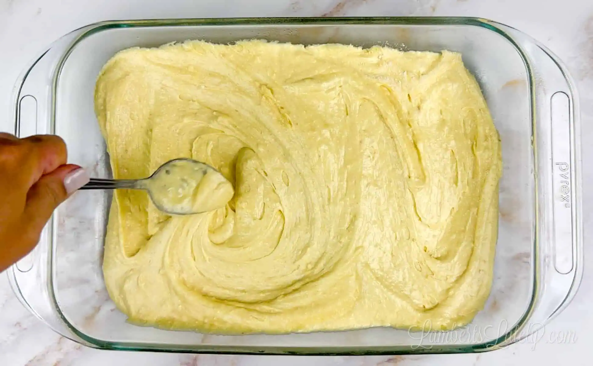 spreading banana cake batter in a pyrex dish.