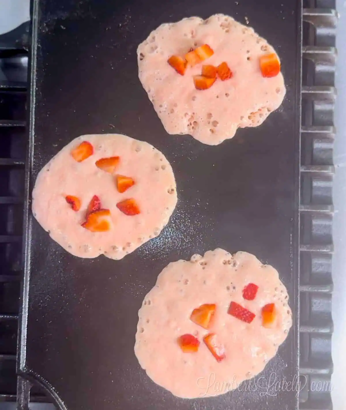 pink pancakes with strawberries on top on a griddle pan.