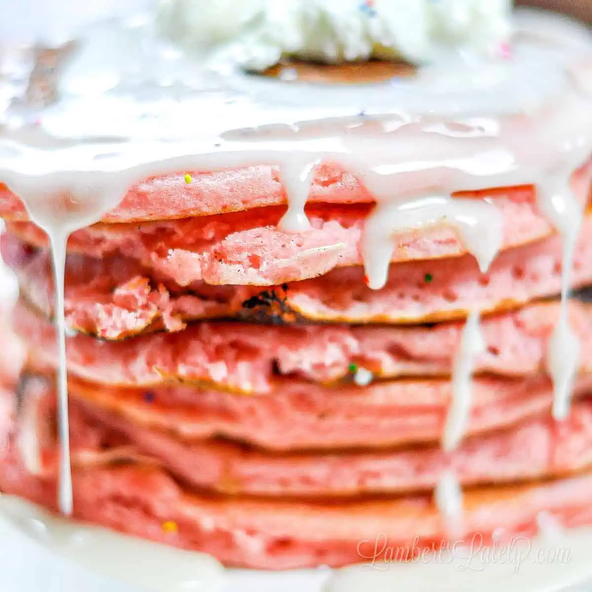 white icing syrup dripping off of of a stack of pink pancakes.