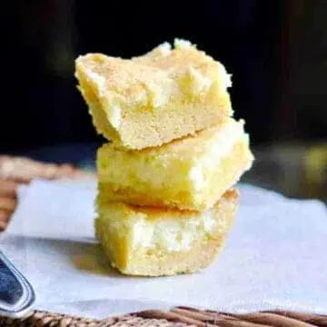 lemon cream cheese bars stacked on a piece of parchment paper.