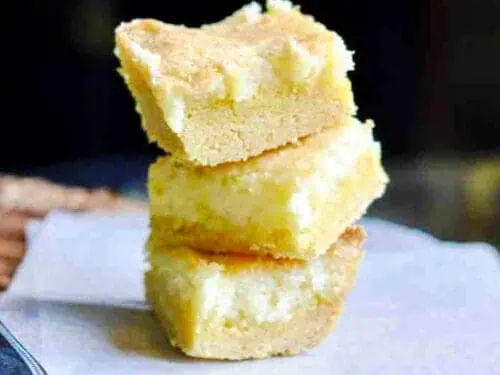 lemon cream cheese bars stacked on a piece of parchment paper.