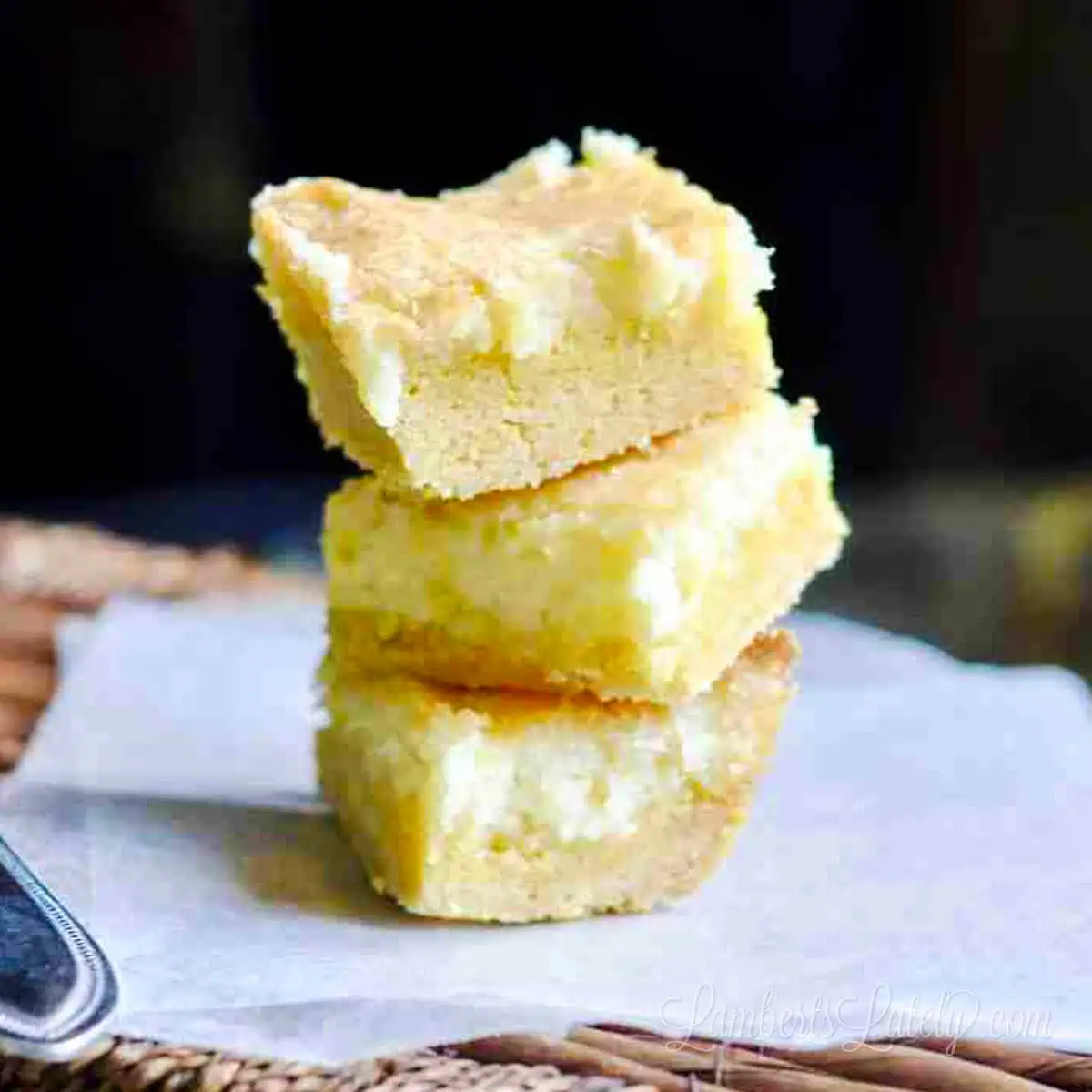lemon cream cheese bars stacked on a piece of parchment paper.