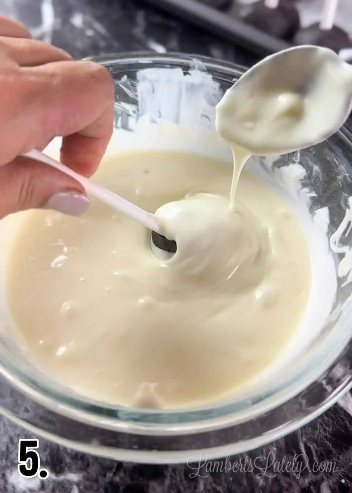 covering oreo cake pop in melted white chocolate using a spoon.