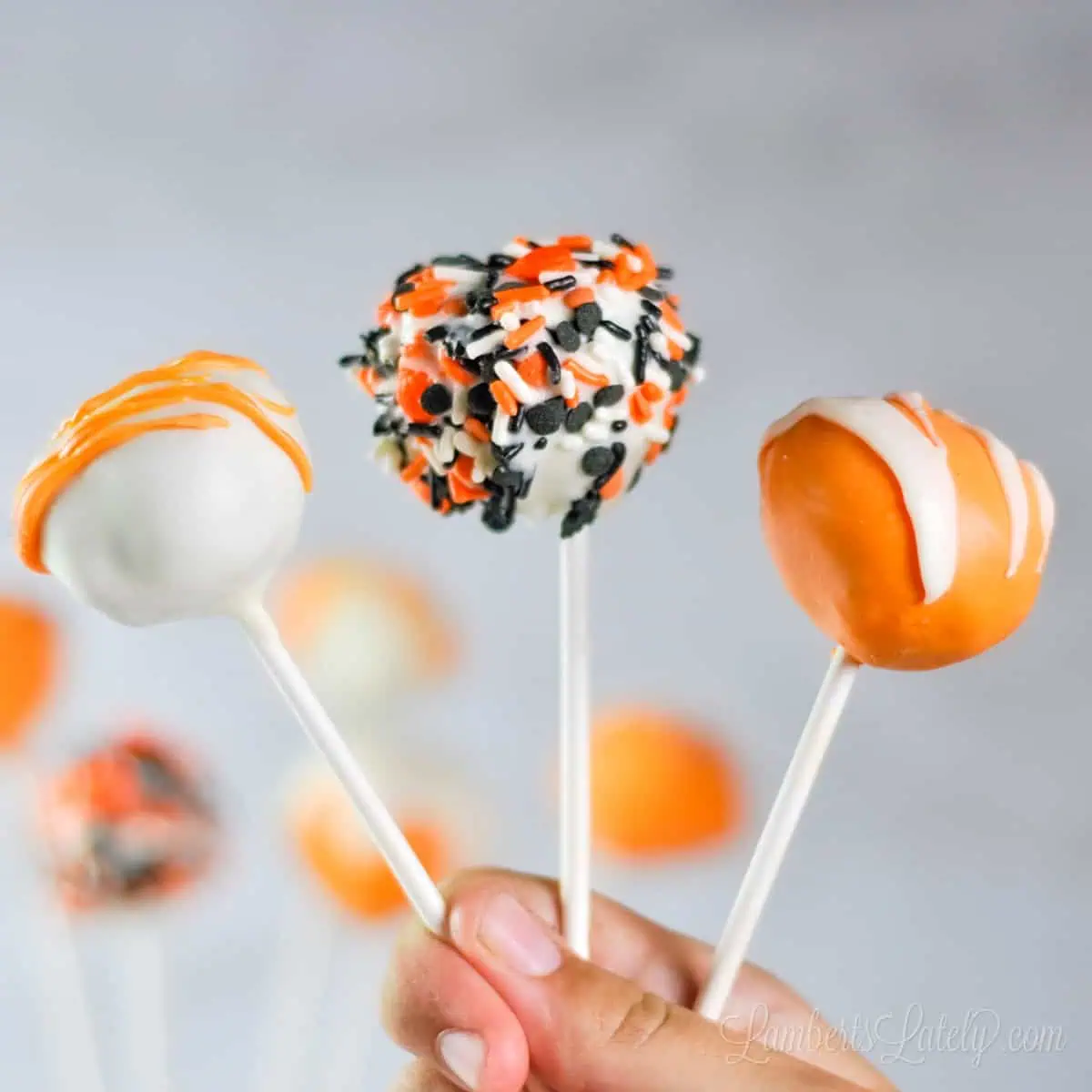 holding 3 pumpkin cake pops with different decorations.