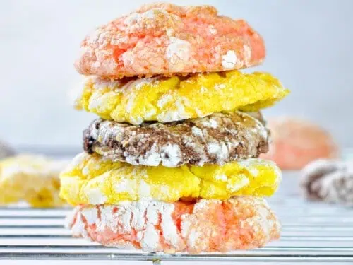 three cool whip cookies (lemon, chocolate, and strawberry) stacked on a wire baking rack.