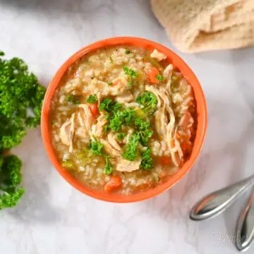bowl of chicken and rice soup with 2 spoons and a bunch of parsley.