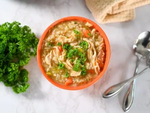 bowl of chicken and rice soup with 2 spoons and a bunch of parsley.