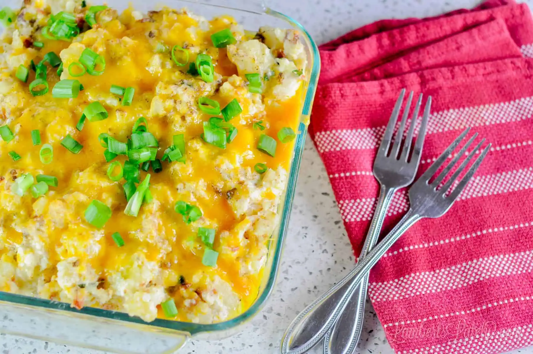 casserole dish of twice baked mashed potatoes, with red kitchen towel and forks.