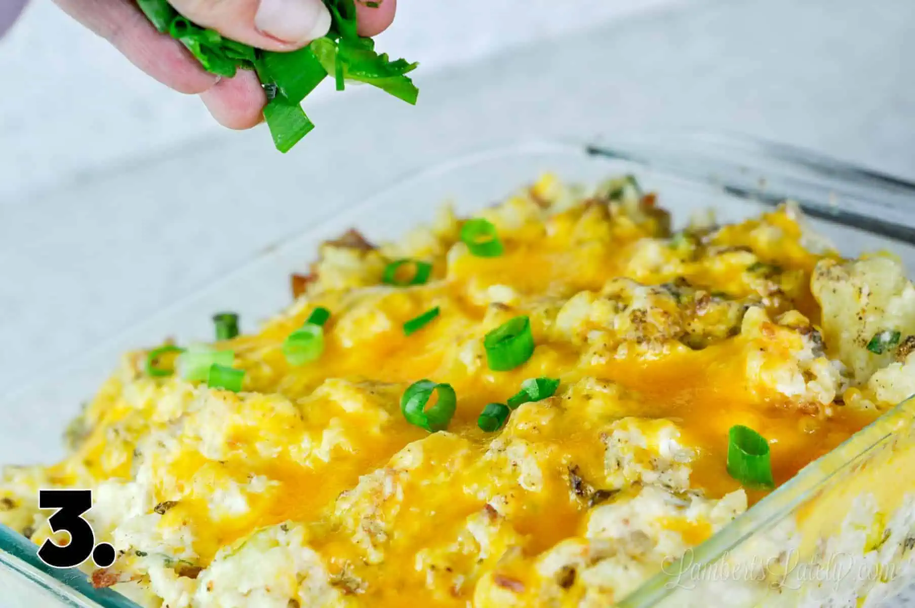 sprinkling green onions on potatoes in a casserole dish.