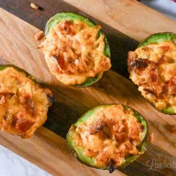 four baked and stuffed avocado halves on a cutting board.