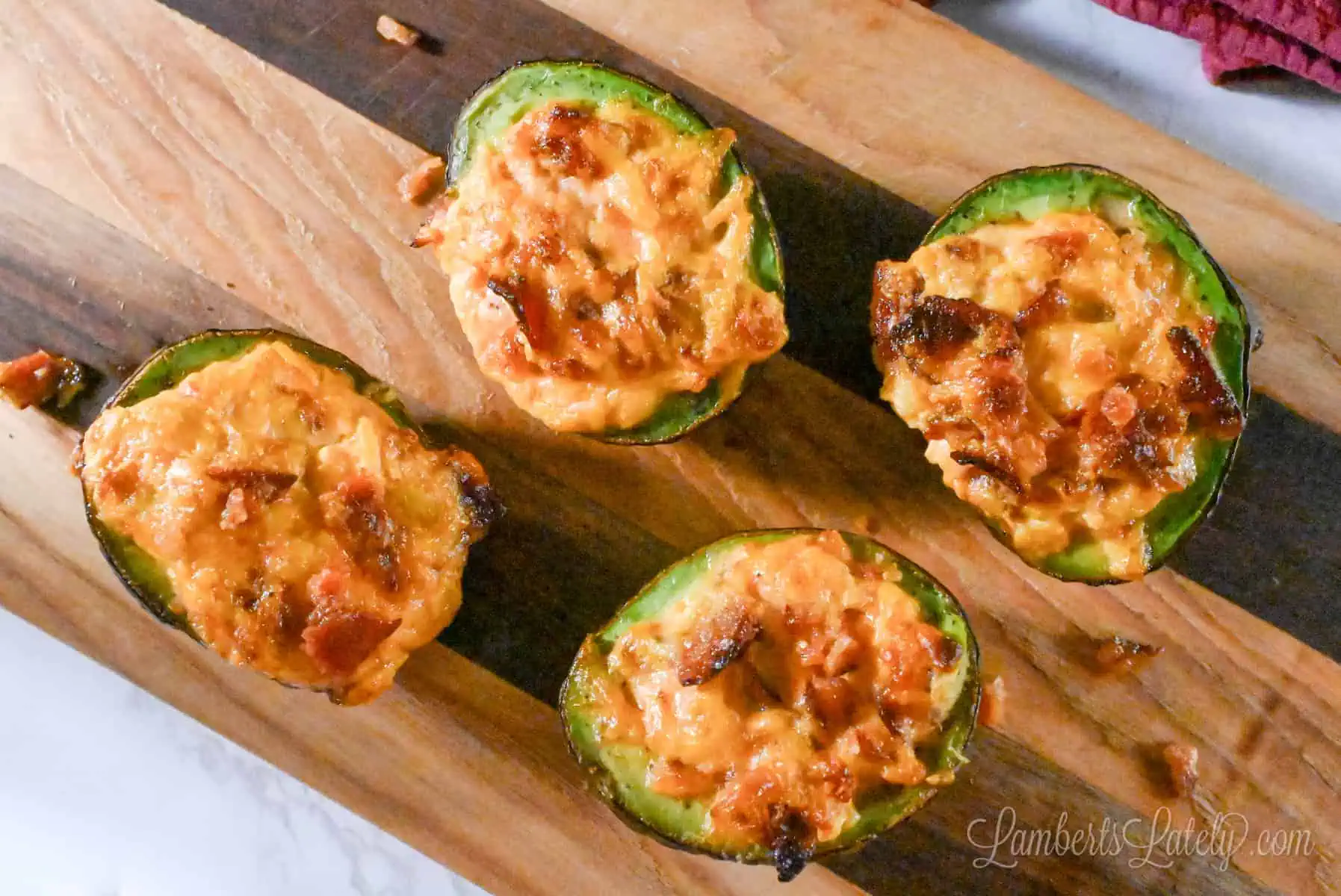 four baked and stuffed avocado halves on a cutting board.