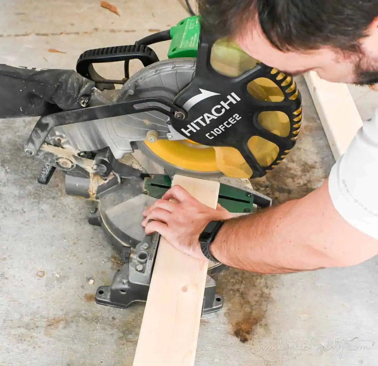 man cutting a piece of wood with a miter saw.