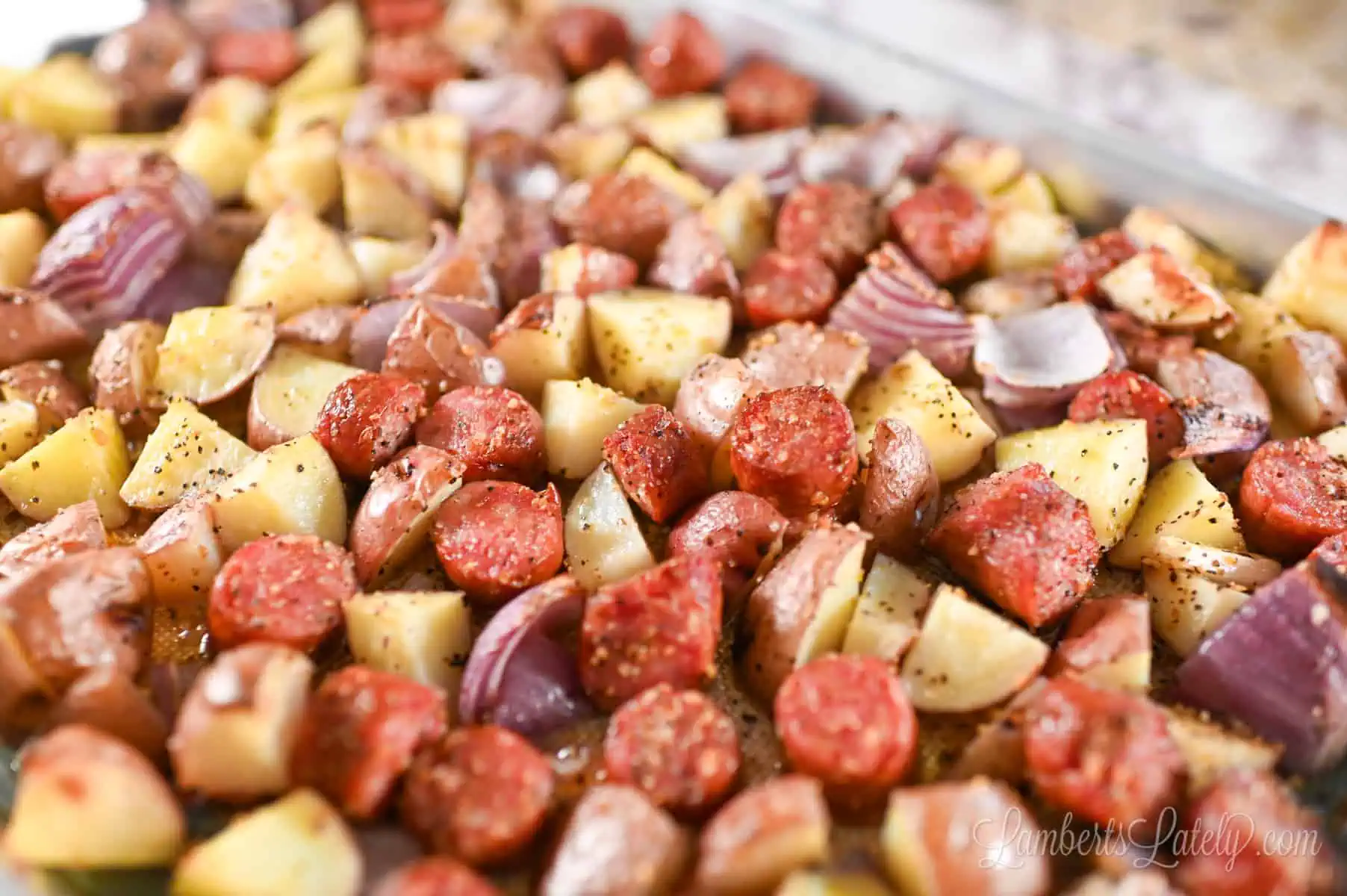 sausage, potatoes, and onion tossed with olive oil and seasoning on a sheet pan.