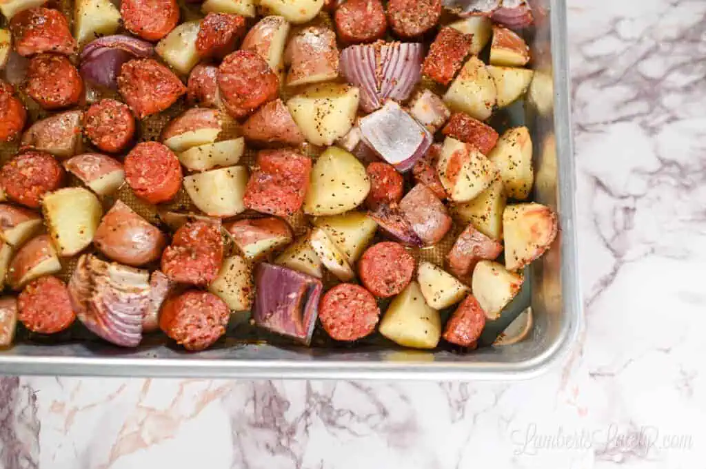 sausage, potatoes, and onion tossed with olive oil and seasoning on a sheet pan.