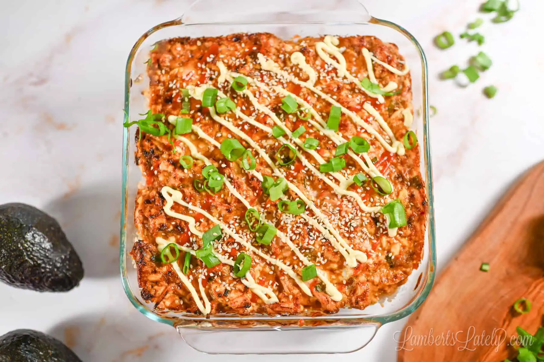 spicy salmon sushi bake in a casserole dish, with a cutting board and avocados.
