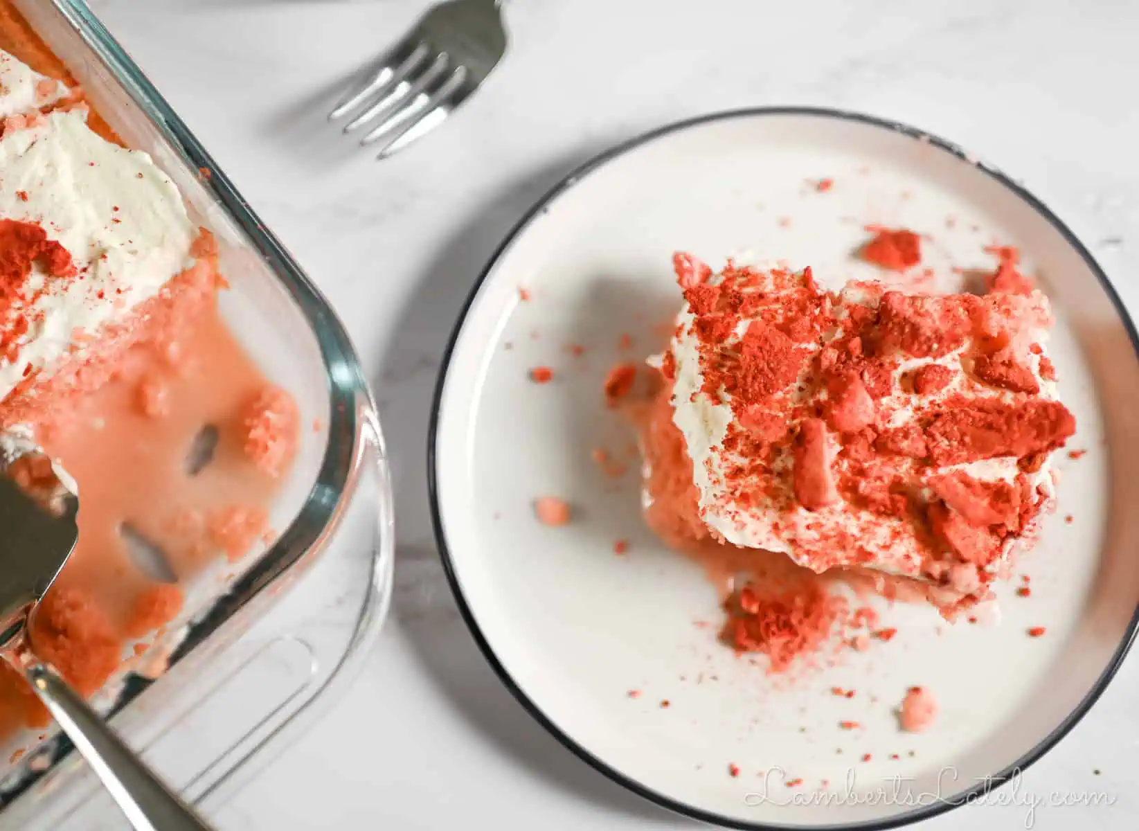 a piece of strawberry tres leches cake on a plate next to the baking dish of cake.