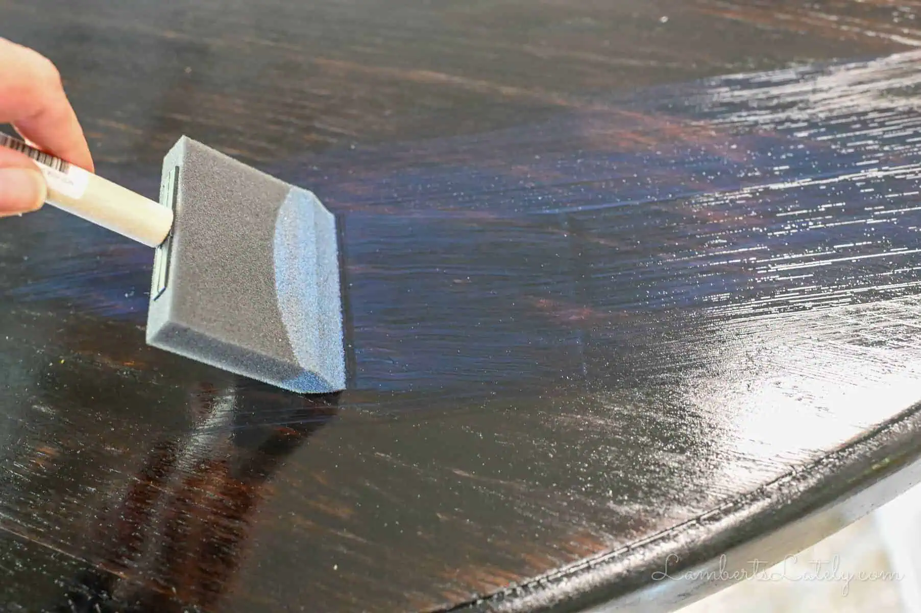 brushing polyurethane onto a stained table with a sponge brush.
