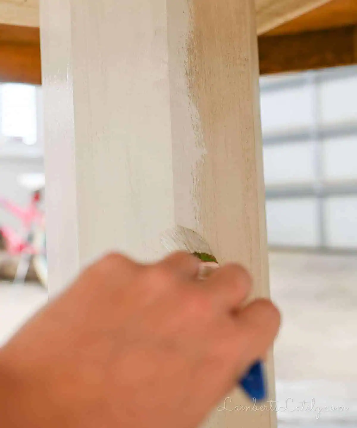painting a light paint on the base of a wood table.