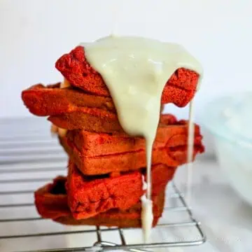 cream cheese glaze poured over top of a stack of red velvet waffles.
