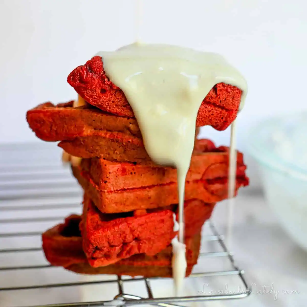 cream cheese glaze poured over top of a stack of red velvet waffles.