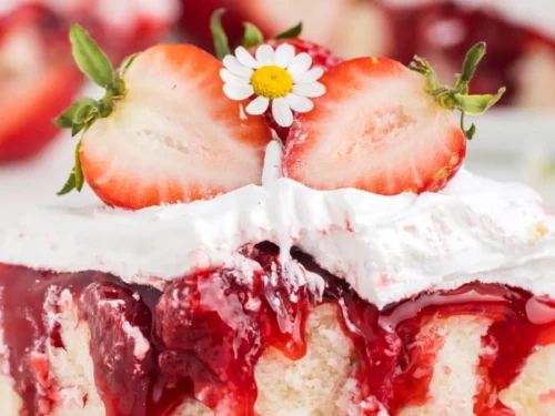 strawberry shortcake poke cake on a plate, topped with strawberries and small flowers.