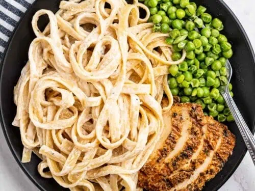 fettuccine alfredo on a plate with meat and peas.