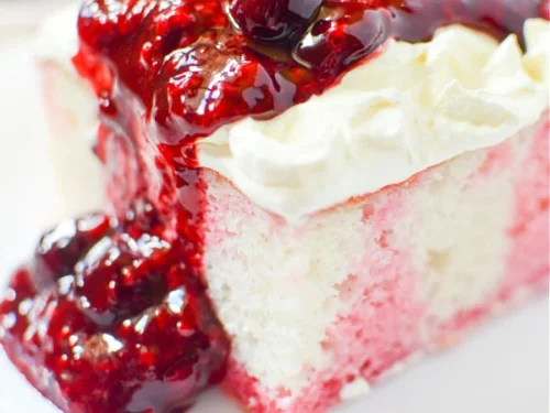 mixed berry poke cake covered in fruit sauce on a plate.