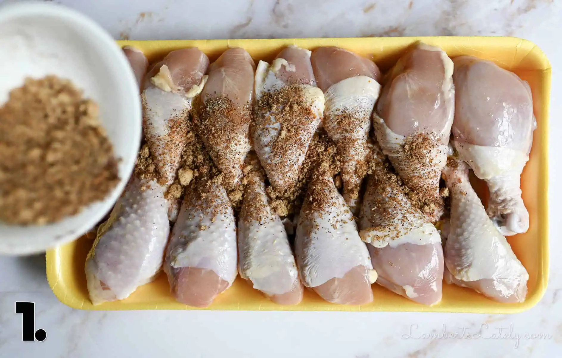 pouring spices over uncooked chicken legs.