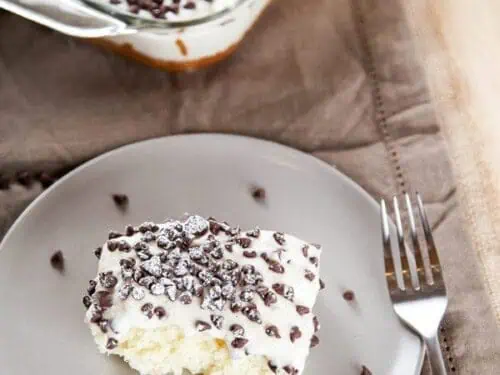 cannoli cake on a plate next to a baking dish.