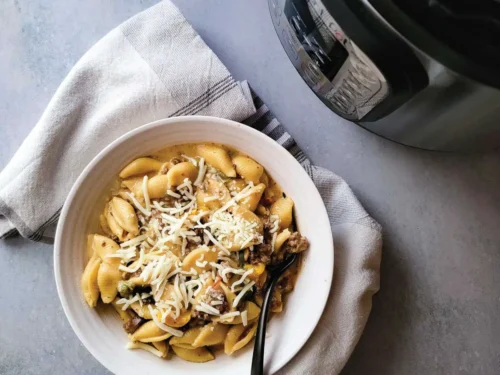 bowl of cheesesteak pasta with a fork, napkin next to bowl, instant pot in background.