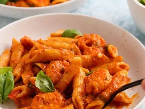 shrimp penne pasta in a bowl topped with basil.