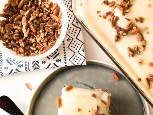 bowl of pecans next to a kentucky butter poke cake, with a plate and a slice of cake.
