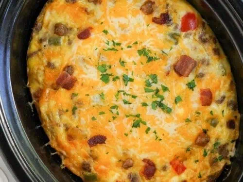 breakfast casserole in a slow cooker, covered in cheese and garnish.