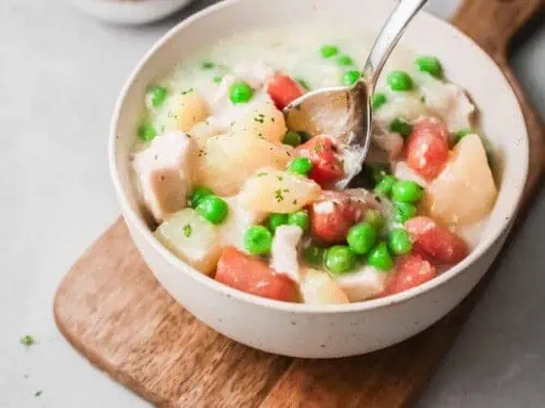 chicken pot pie in a bowl on top of a cutting board, with a spoon.