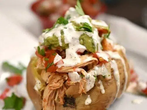 taco sweet potato on a plate, covered in sour cream and guacamole.
