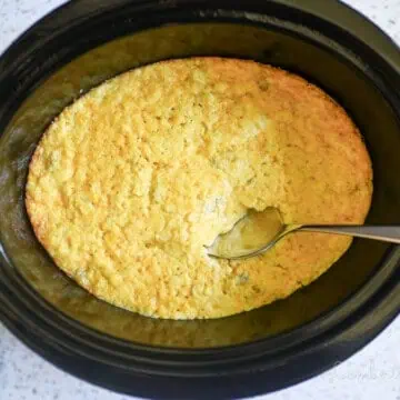 corn casserole in a crock pot, with spoon in casserole.