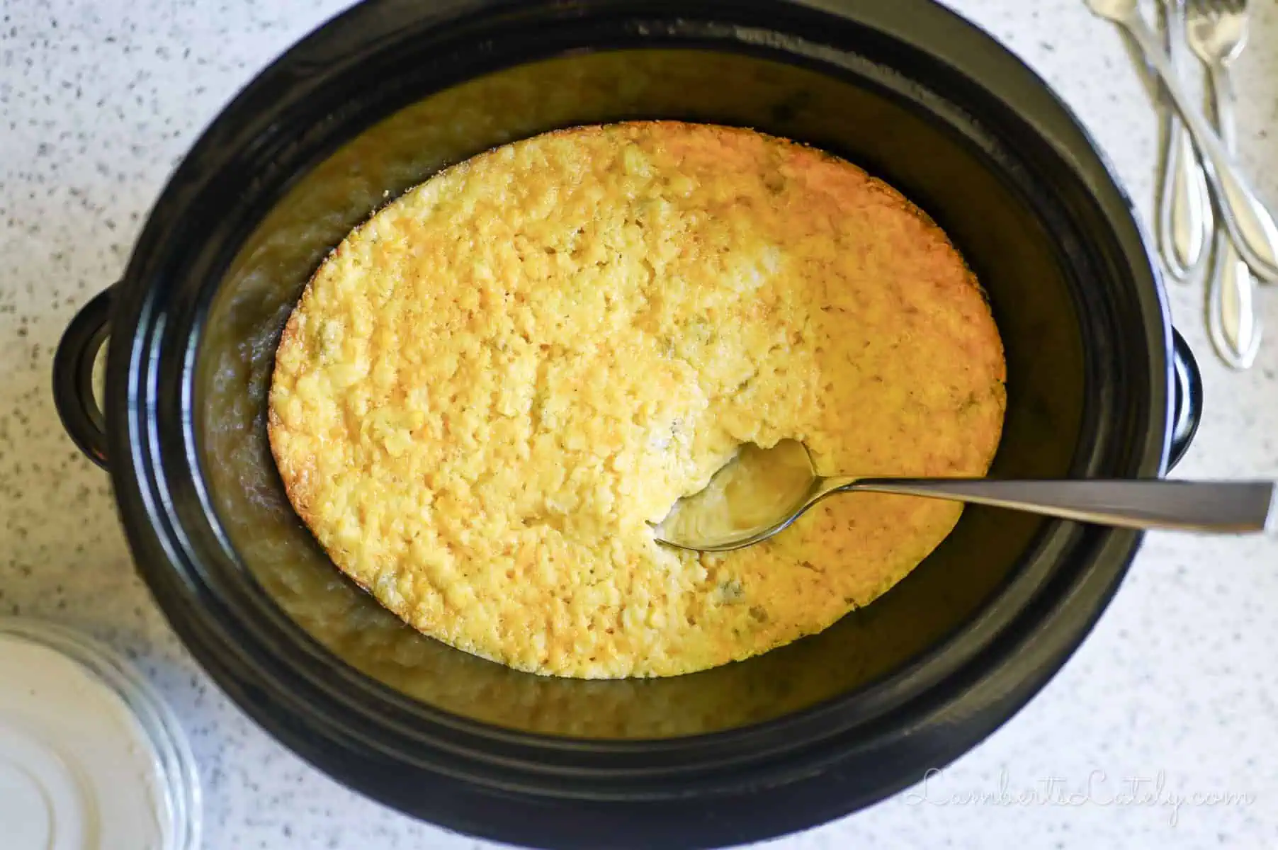 corn casserole in a crock pot, with spoon in casserole.