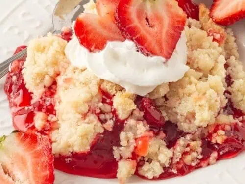Strawberry Cream Cheese Dump Cake in a bowl, topped with whipped cream and fresh strawberries.